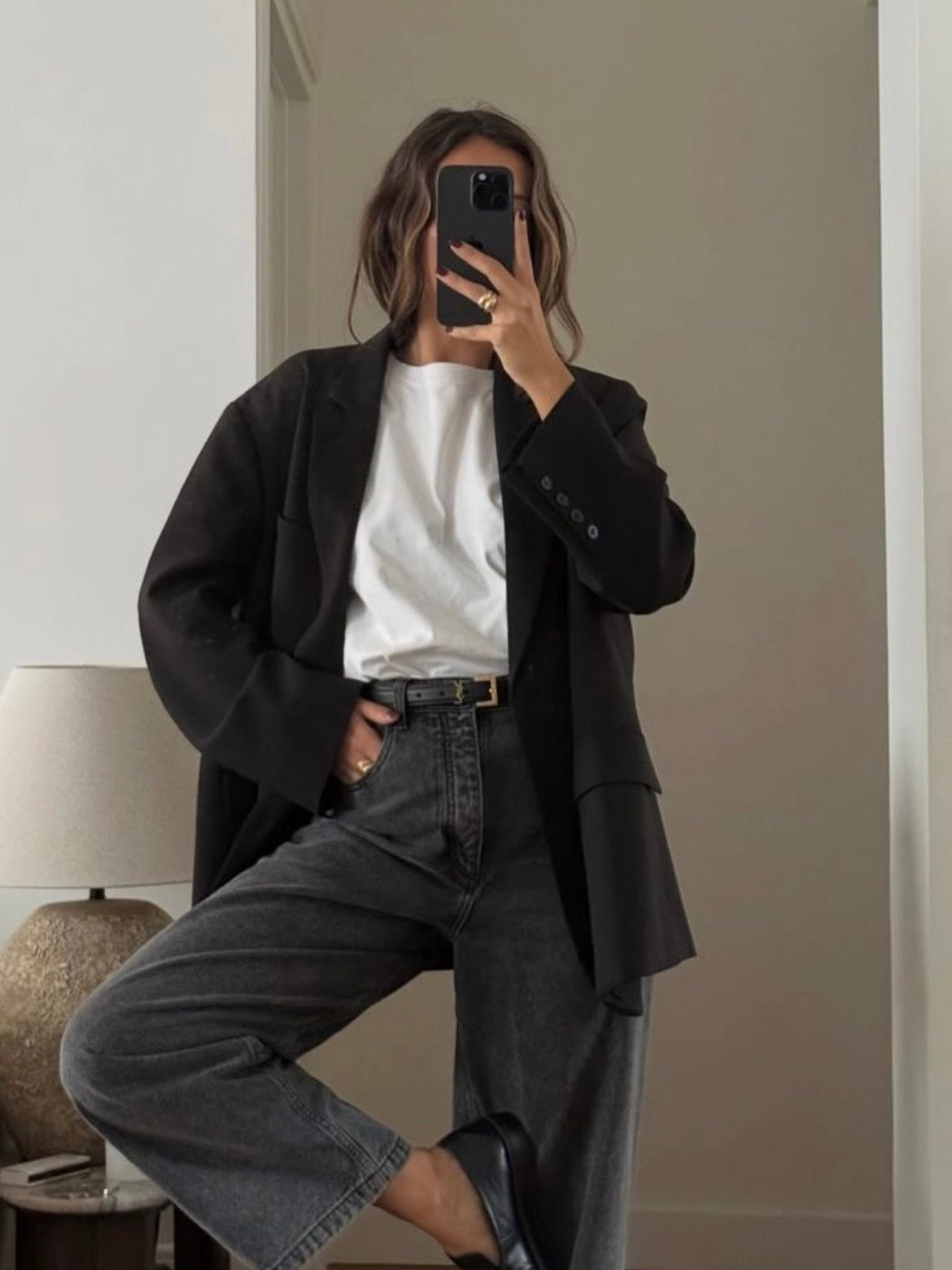 Person in a black blazer, white t-shirt, and grey jeans taking a mirror selfie.