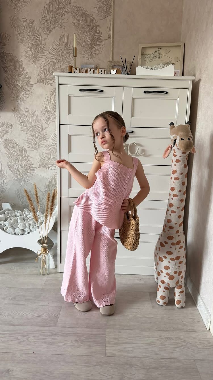 Young girl wearing a pink two-piece outfit posing next to a plush giraffe.