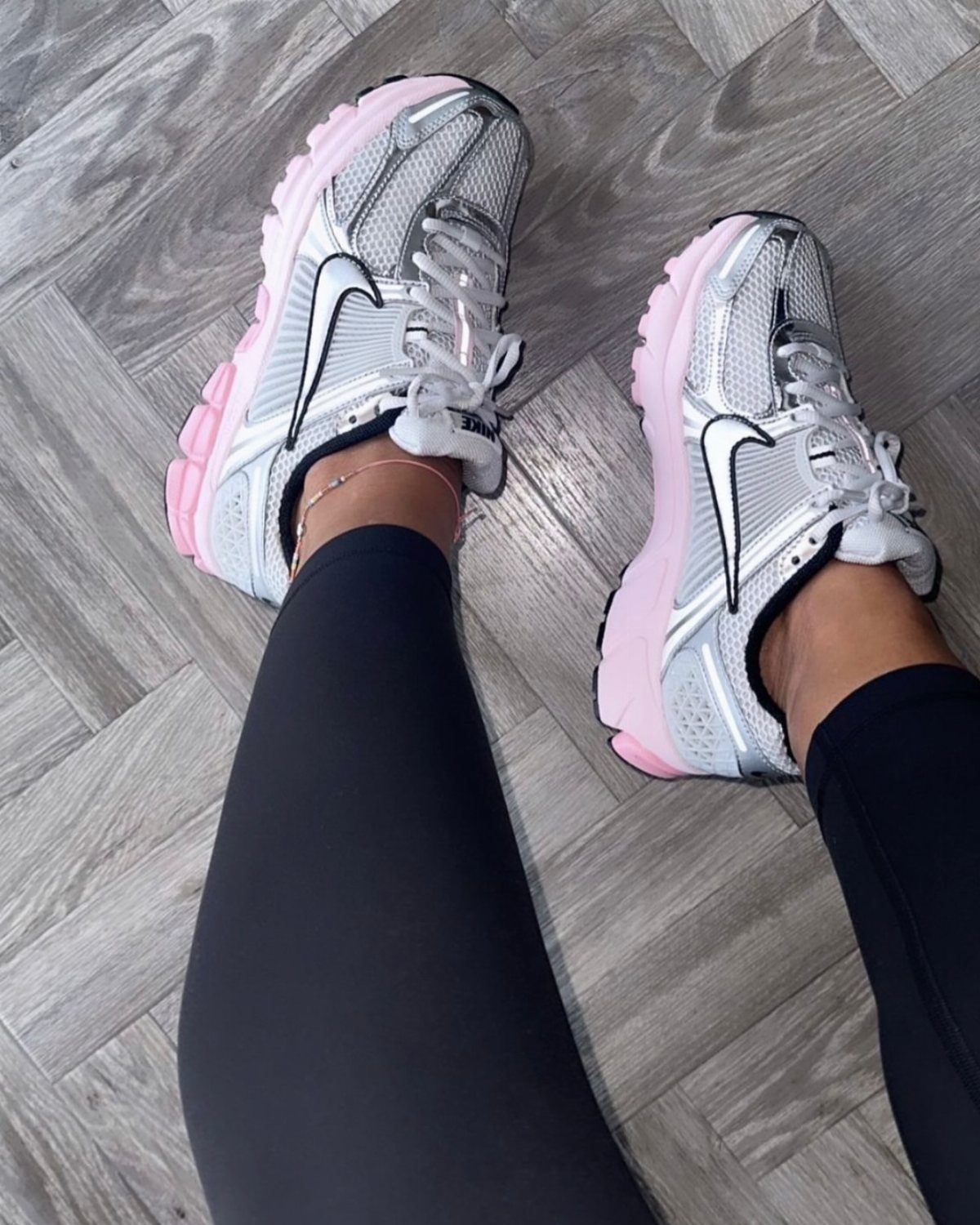 Pink and White Designer Sneakers: 5 Pairs for Women 2 Pink and white Nike Zoom Vomero 5 sneakers worn with black leggings on wooden flooring.