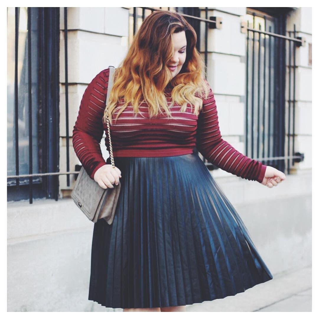 13 Plus Size Brunch Outfit Ideas for Every Style 3 Woman wearing a burgundy knit sweater and black pleated midi skirt outdoors.