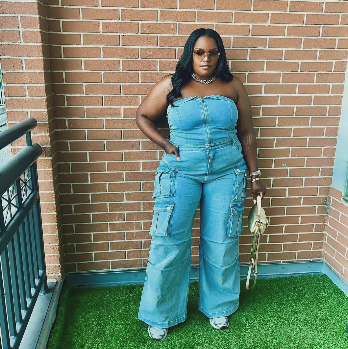 13 Plus Size Brunch Outfit Ideas for Every Style 12 Plus-size woman in a strapless denim cargo jumpsuit standing against a brick wall.
