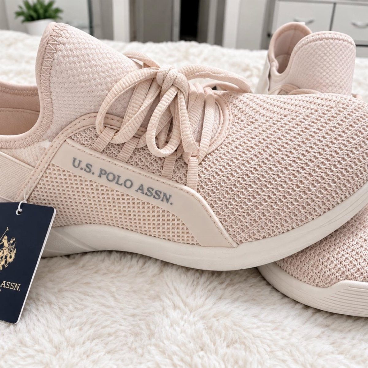 Light pink mesh sneakers with U.S. Polo Assn. branding on white fluffy rug