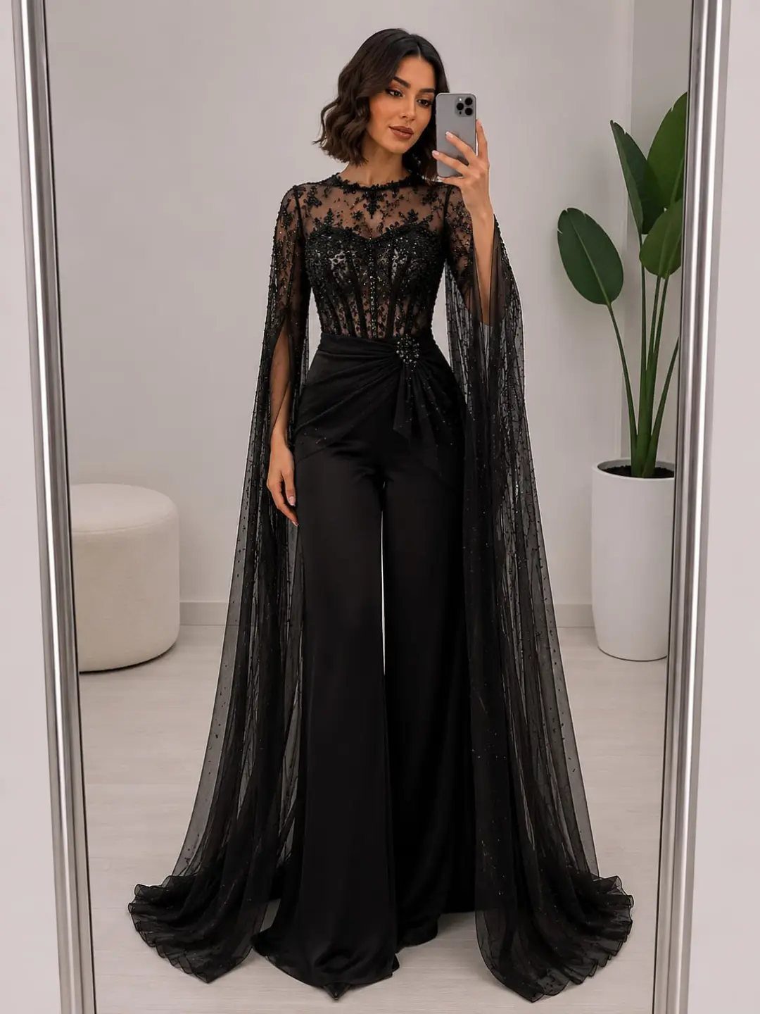 Woman in a formal black lace jumpsuit with a long sheer cape