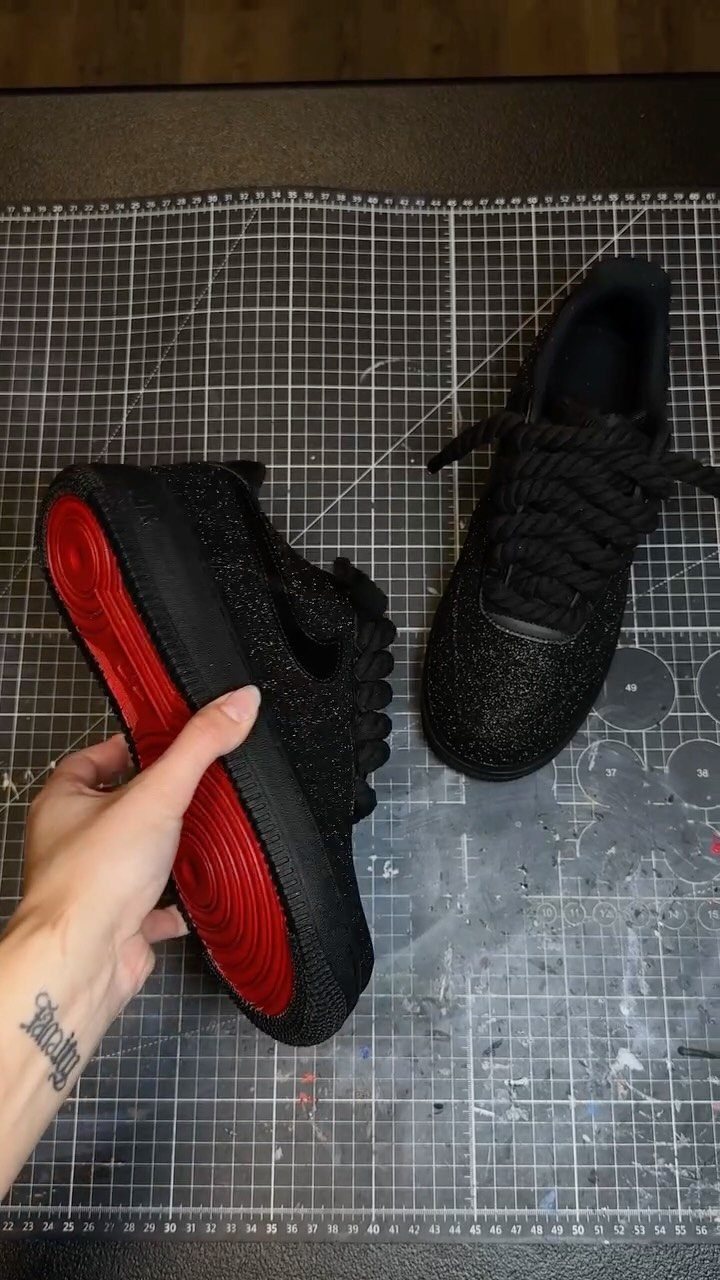Black glittery custom sneakers with red soles resting on a grey grid mat.