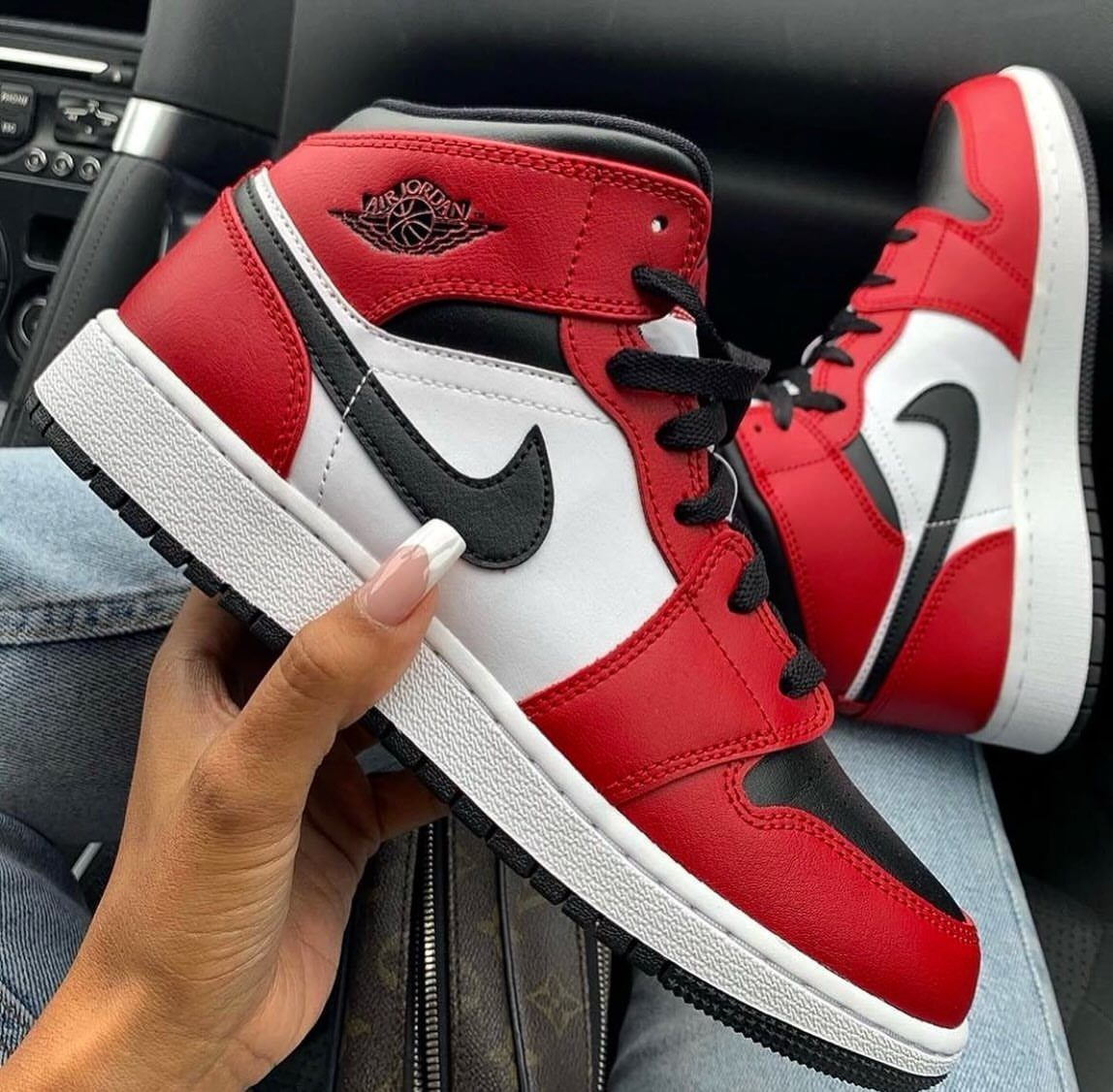 Red, white, and black Nike Air Jordan 1 Mid sneakers held by a hand.