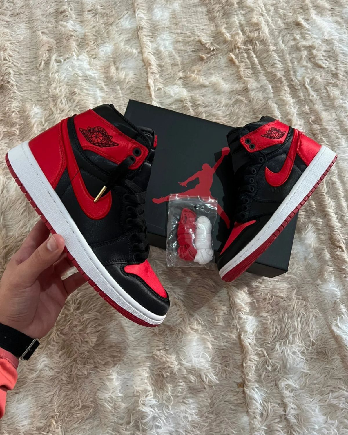 Red and black Nike Air Jordan high-top sneakers on a white fluffy rug.