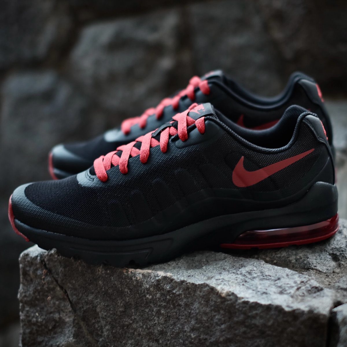 Black Nike Air Max Invigor sneakers with red accents on a stone ledge.
