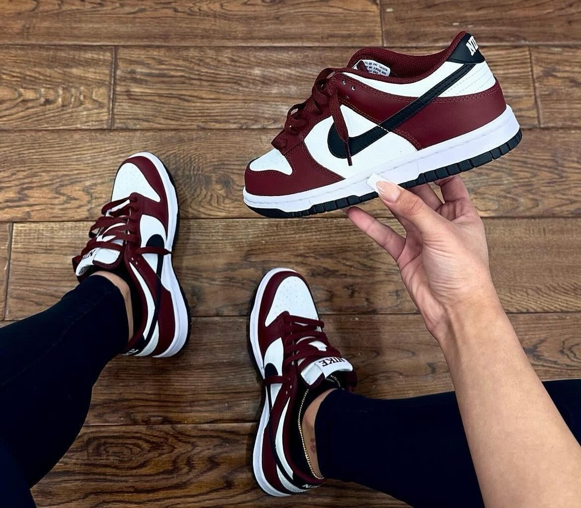 Red and white Nike Dunk Low sneakers on feet and held by hand.