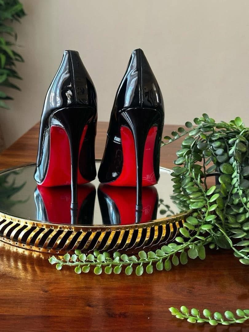 Black patent leather high heels with red soles on a mirrored gold tray.
