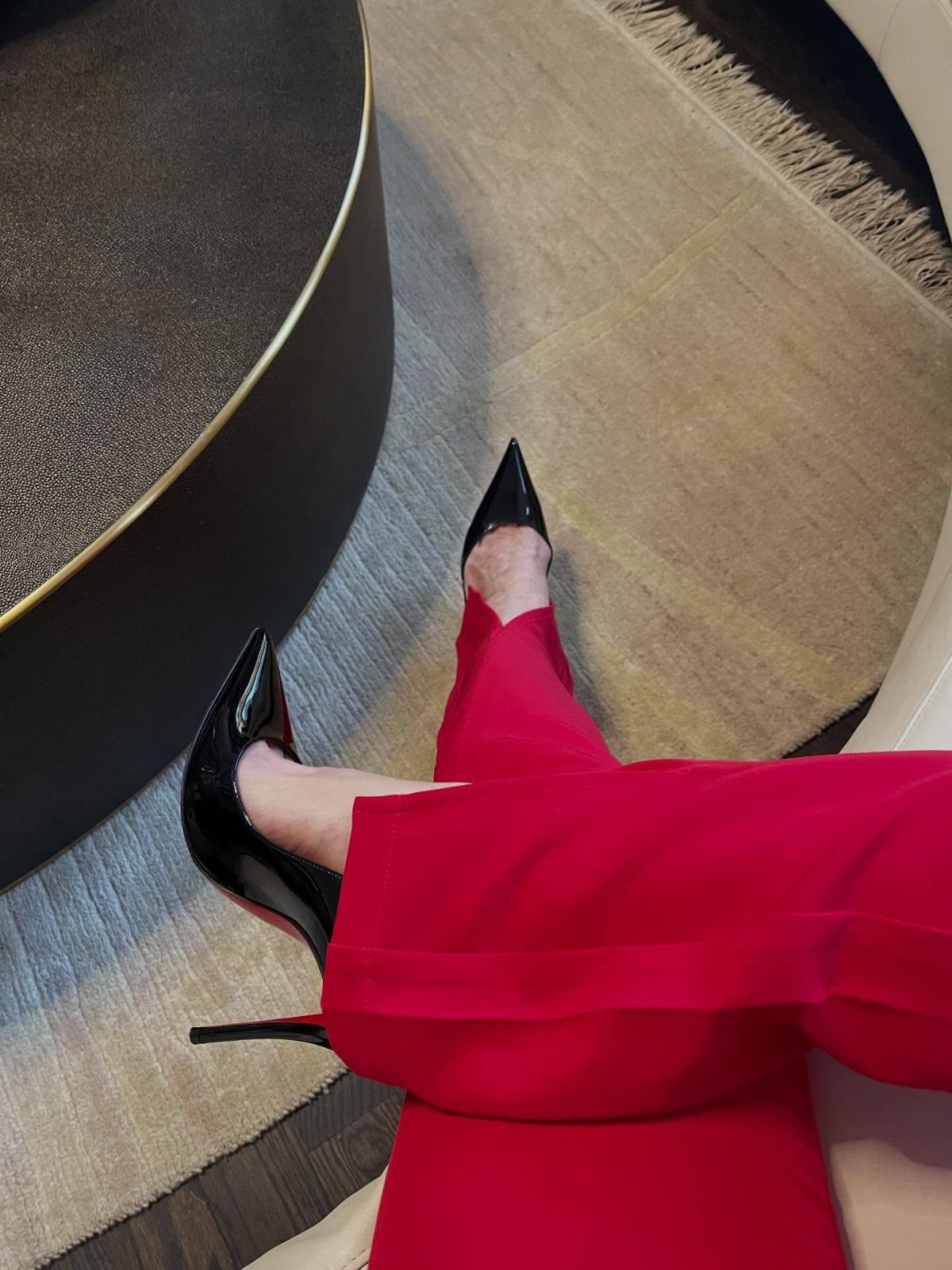 Black pointed-toe stiletto heels with red soles and red trousers on beige carpet