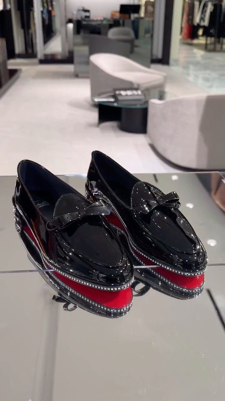 Black patent leather loafers with signature red soles and silver studs on display.