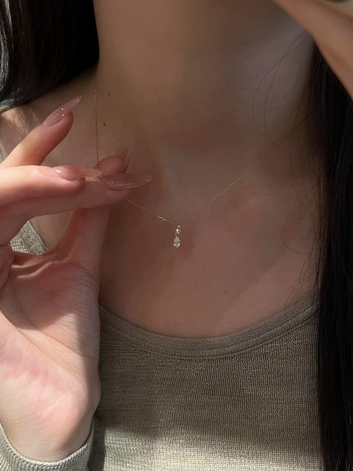 Thin gold necklace with a small teardrop diamond pendant on a person's neck