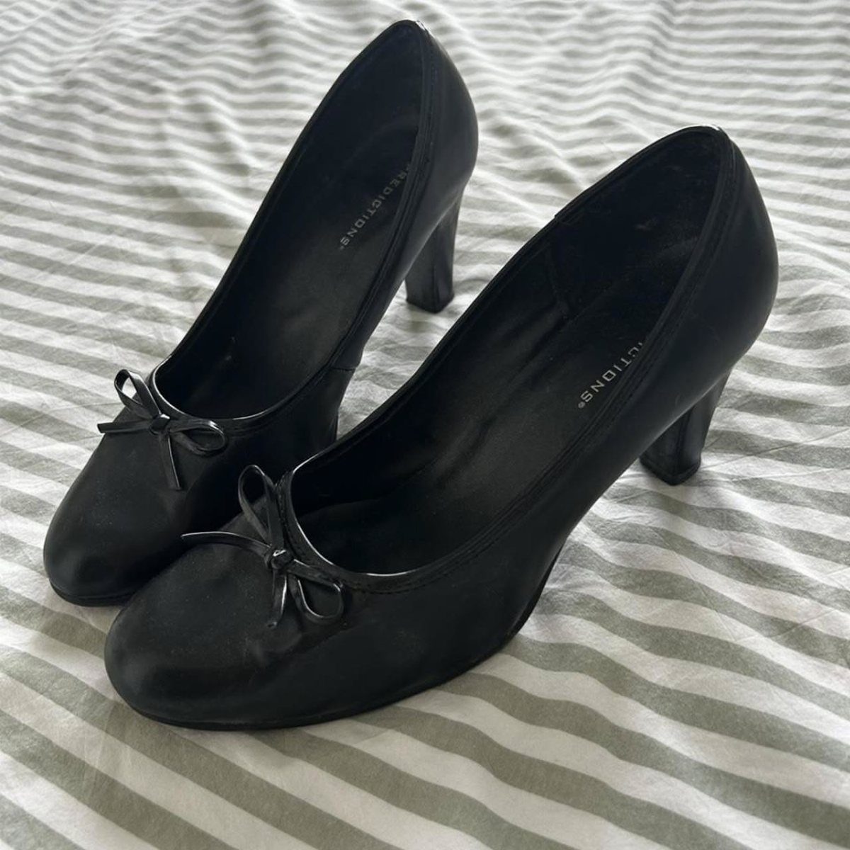 Black round toe kitten heels with small bows on a striped background