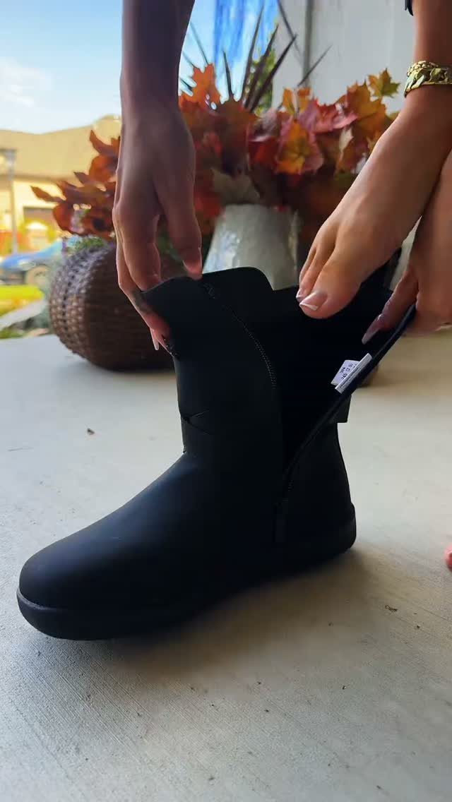Black suede ankle boot held by hands on a table with autumn leaves.