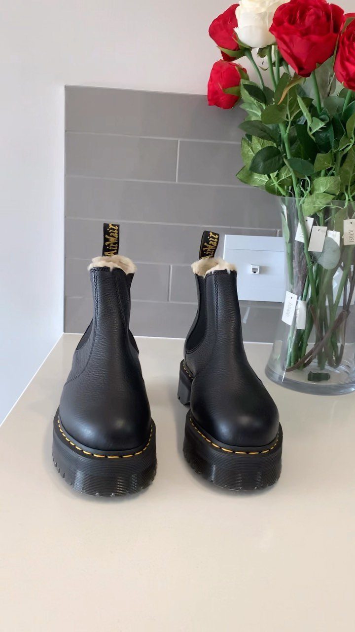 Black leather platform Chelsea boots with fur lining and yellow stitching near roses.