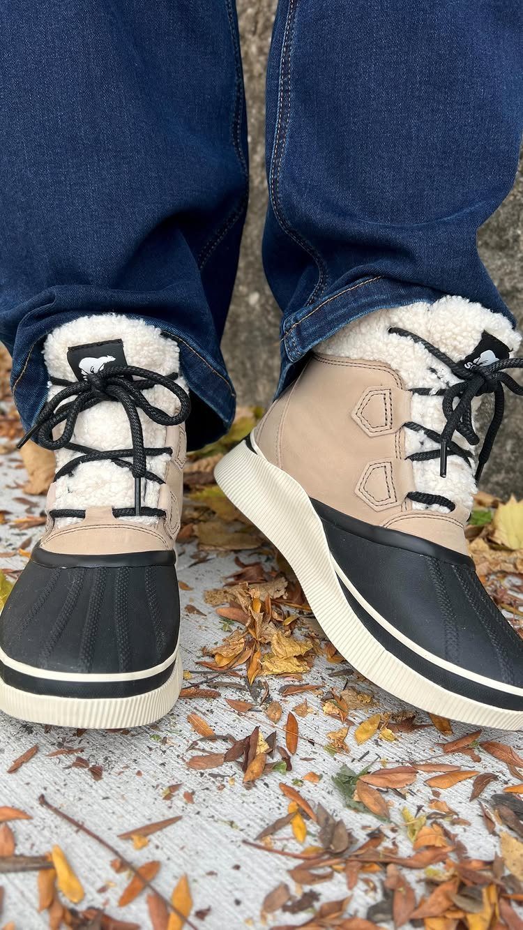 Tan and black waterproof boots with white fur lining on a leaf-covered ground.