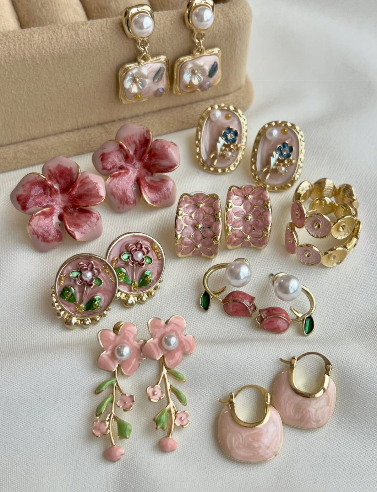 9 Soft Femme Style Ideas with Ruffles, Knits and Pearls 5 Assorted pink floral and pearl jewelry arranged on a white fabric background.