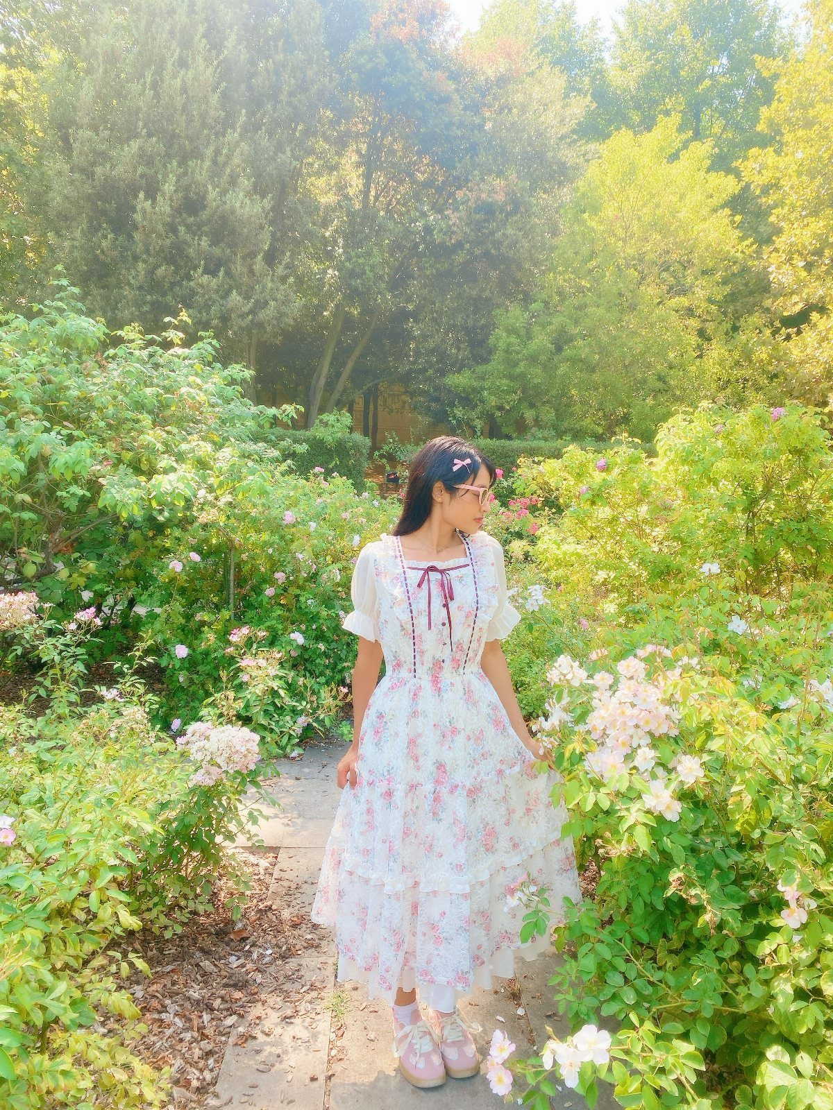 9 Soft Femme Style Ideas with Ruffles, Knits and Pearls 1 Woman in a white floral dress standing among white roses in a garden.