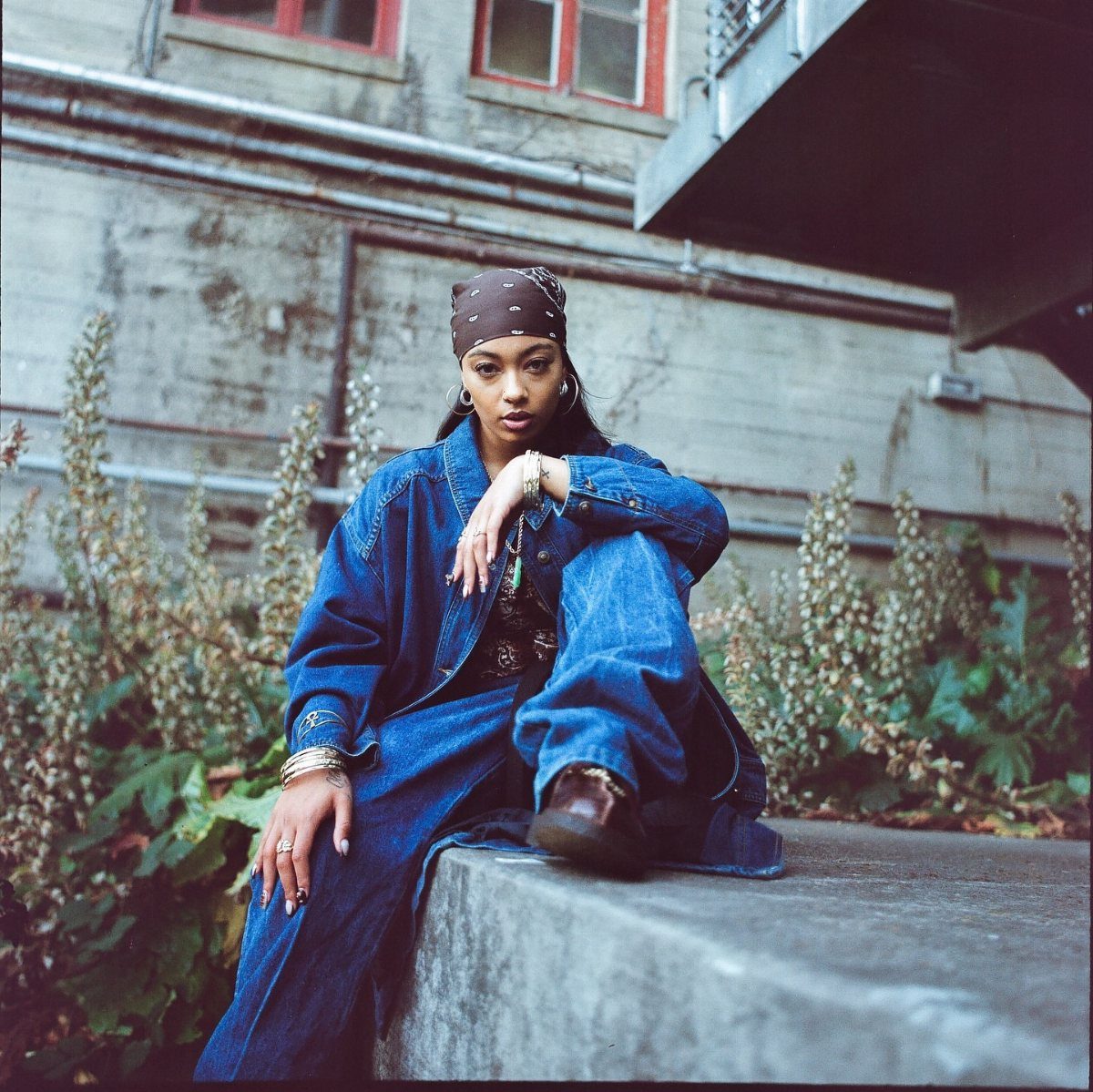 Woman wearing oversized denim jacket and pants with a brown bandana headwrap.
