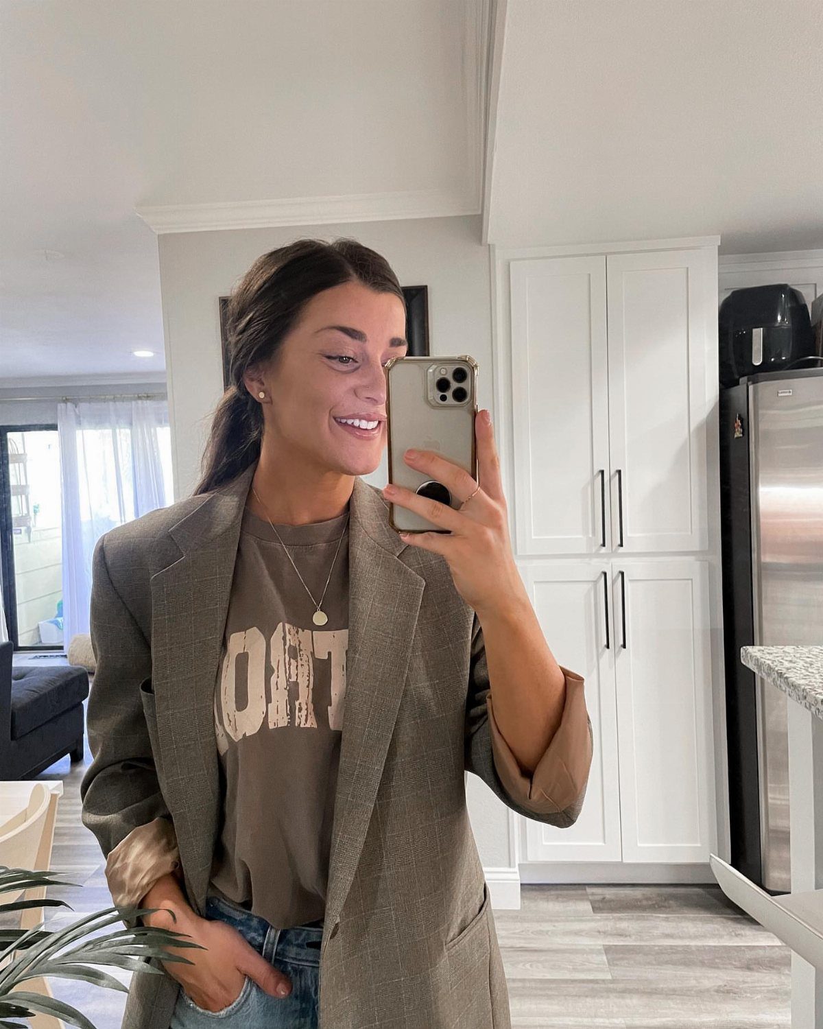 Woman wearing an oversized brown blazer and graphic tee taking a mirror selfie.