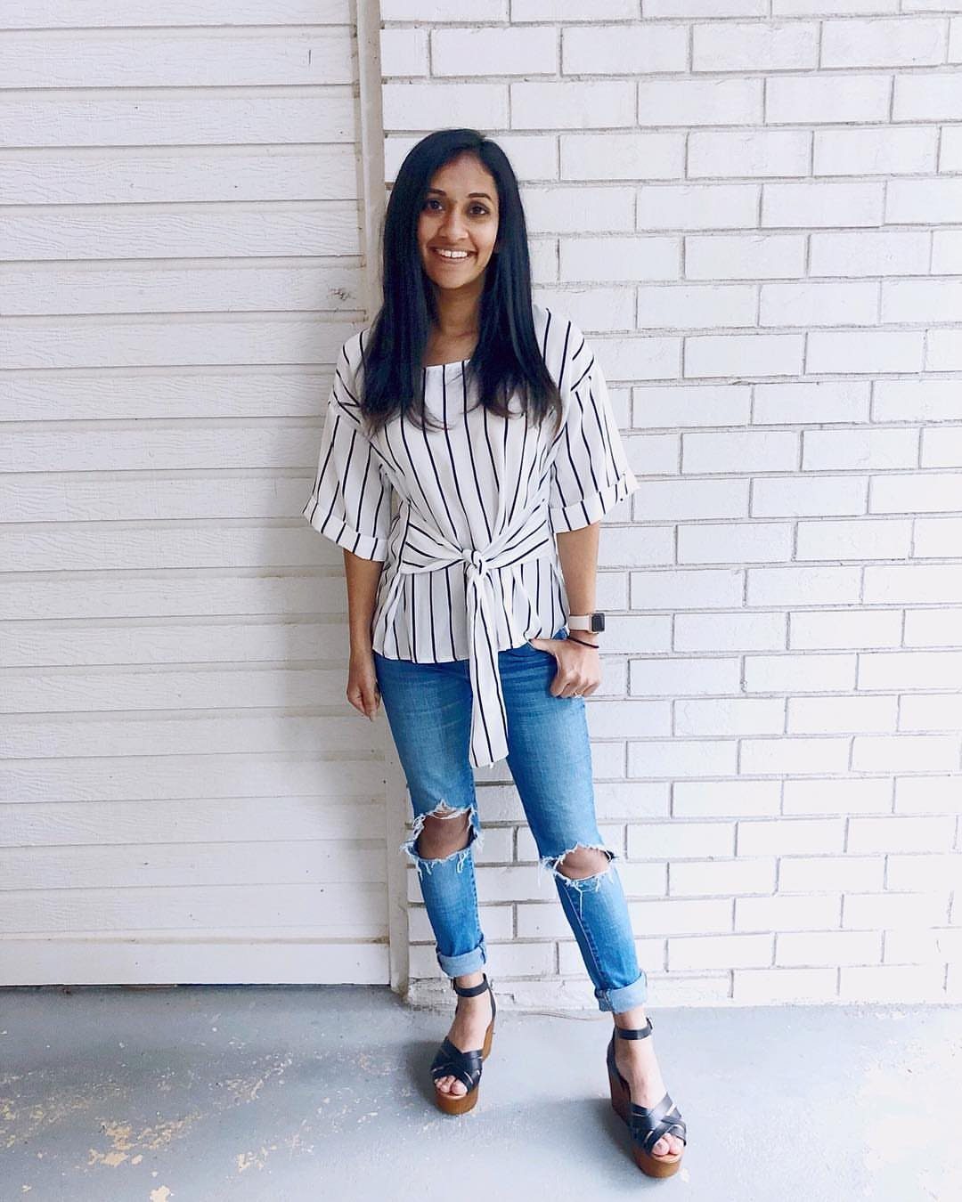 Woman wearing a striped tie-front top with a defined waist and ripped jeans.