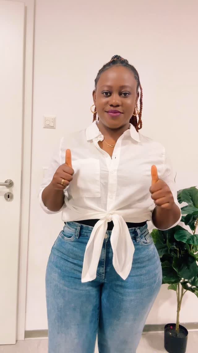 Woman wearing a white button-down shirt tied at the waist and blue jeans.