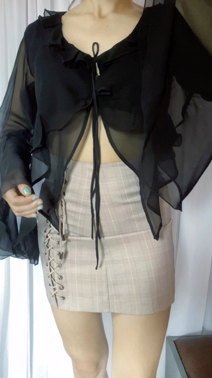 Sheer black tie-front top with ruffles paired with a beige plaid mini skirt.