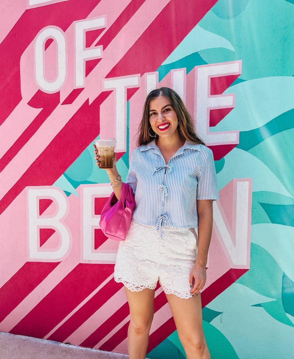 Woman wearing a blue striped tie up top and white lace shorts.
