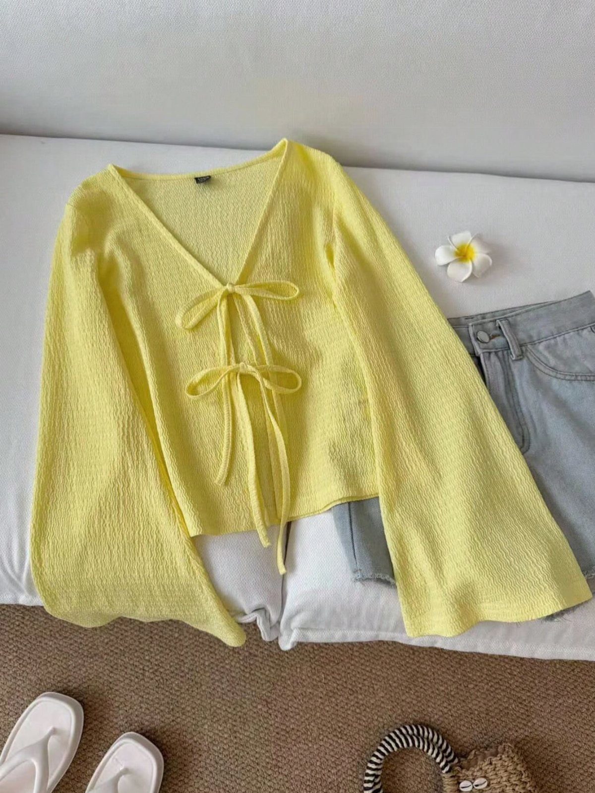 Yellow long-sleeved tie up top laid flat with light blue jeans and sandals.