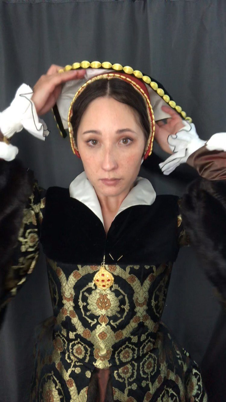 Woman wearing a gold and black Tudor period dress with a French hood.