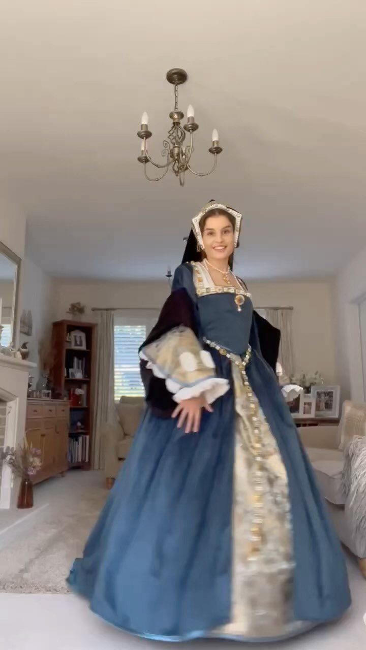 Woman wearing a blue and gold Tudor period dress and gable hood indoors.