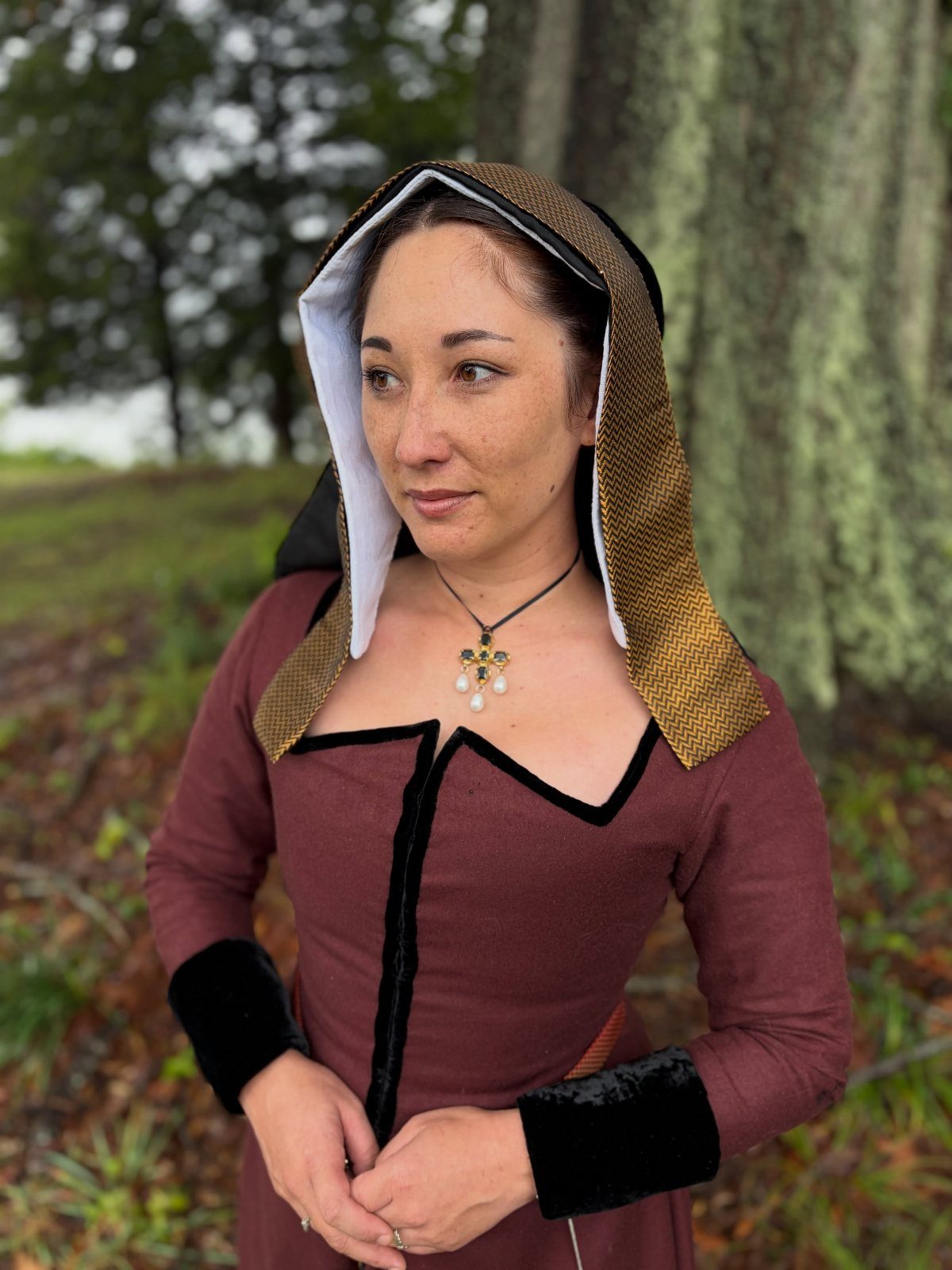 Woman wearing a gold decorative hood and maroon Tudor period dress outdoors.