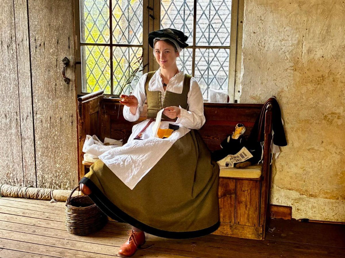 Woman in Tudor period dress sitting on a wooden bench by a window