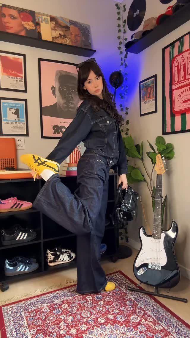 Woman wearing a dark denim jacket and baggy jeans with yellow sneakers.