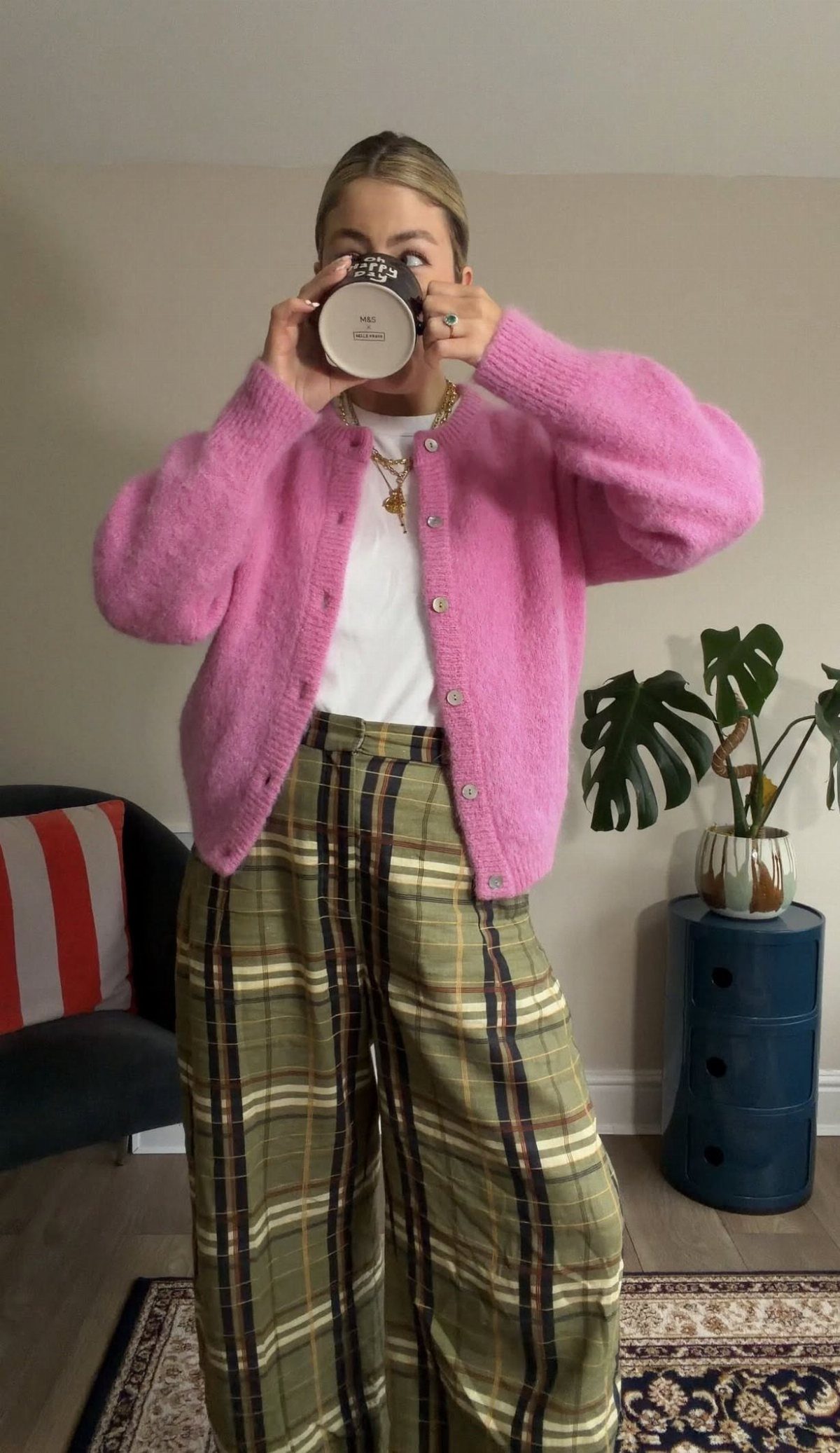Person wearing a pink fuzzy cardigan and olive green plaid wide-leg trousers.