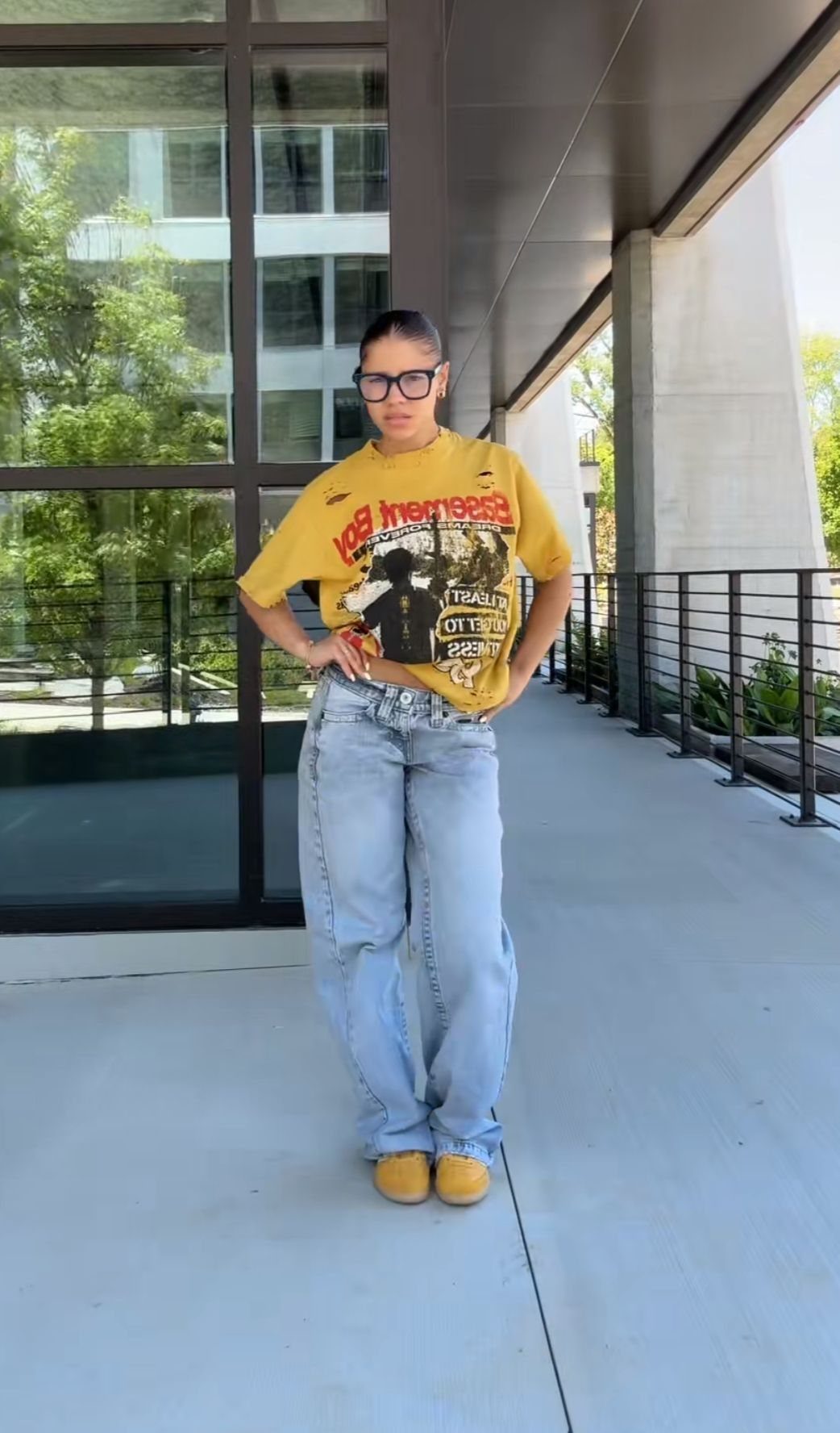 Person wearing a yellow graphic tee and baggy light blue jeans on a balcony