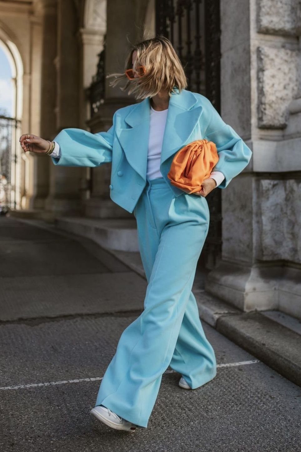 Person in an oversized light blue suit with a bright orange clutch bag.