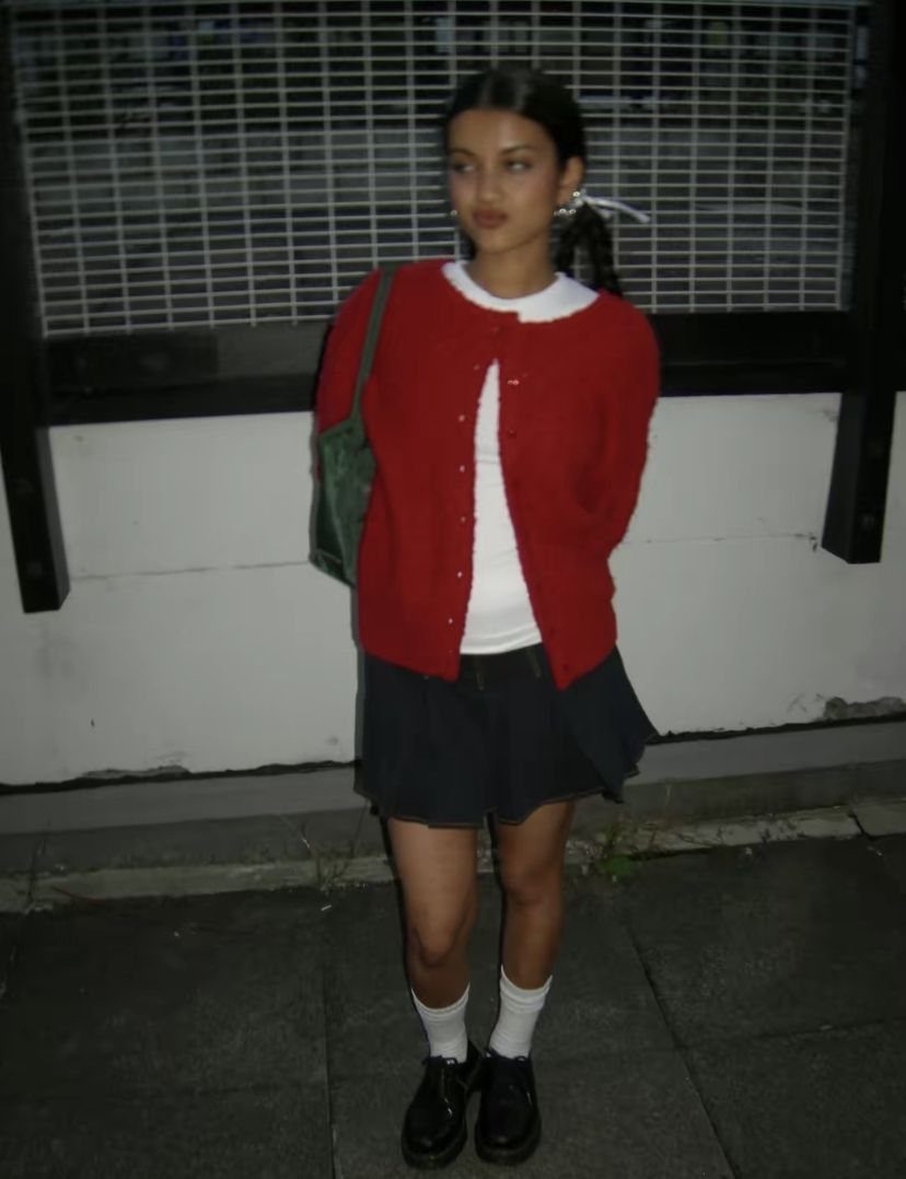 Person wearing a red cardigan, white shirt, and navy pleated mini skirt.