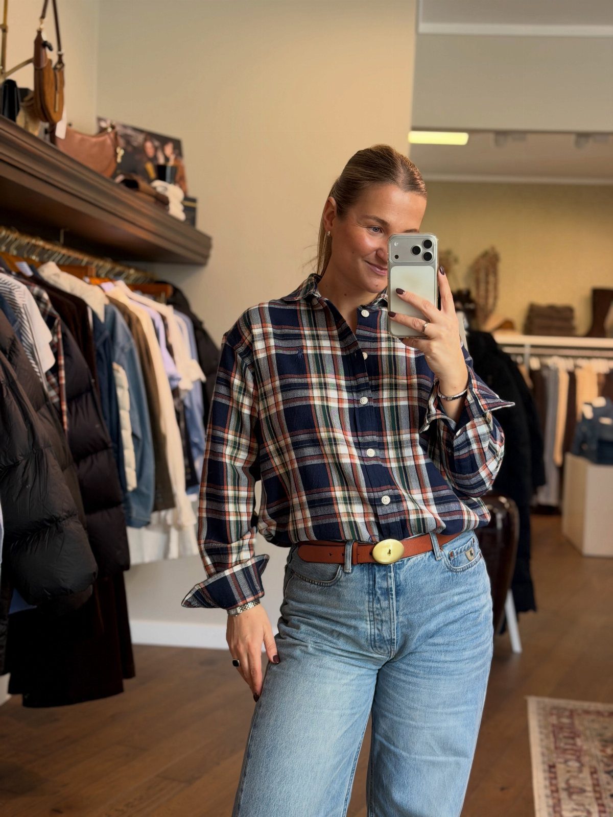 Woman wearing a plaid button-down shirt and blue jeans in a clothing store.