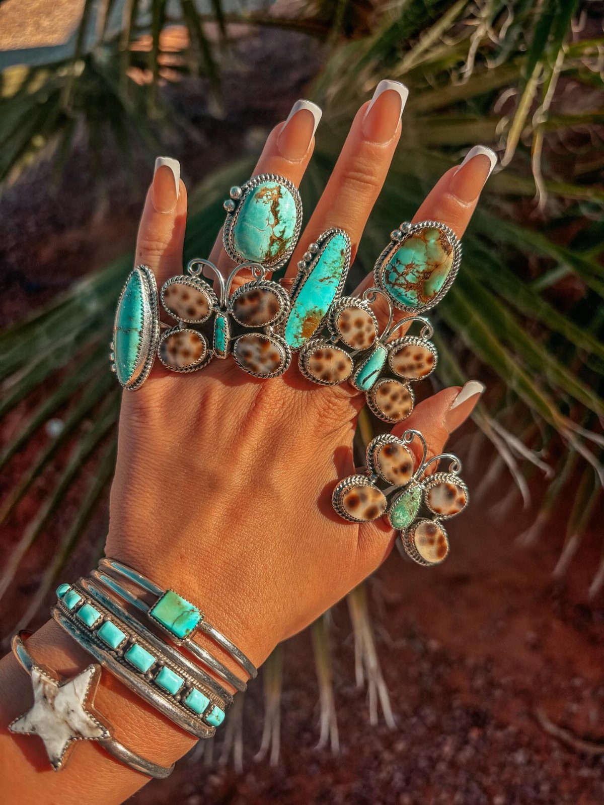 Hand wearing silver rings and bracelets with turquoise and brown stones in desert setting