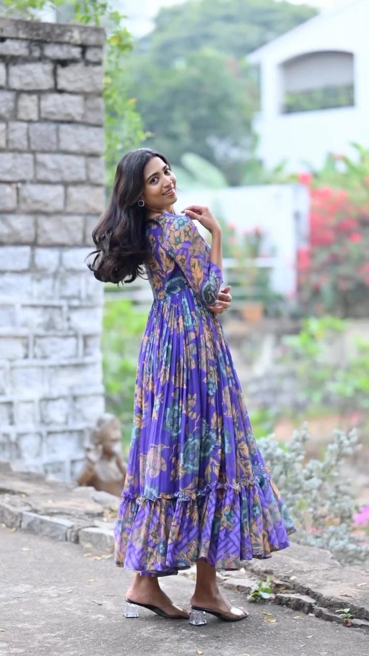 Woman wearing a long purple floral print dress standing by a stone wall