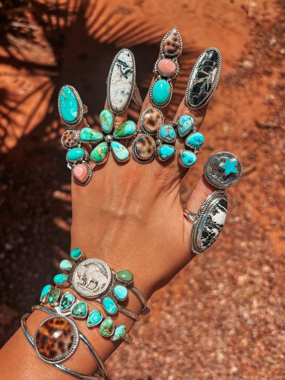Hand and wrist wearing multiple silver rings and bracelets with turquoise stones.