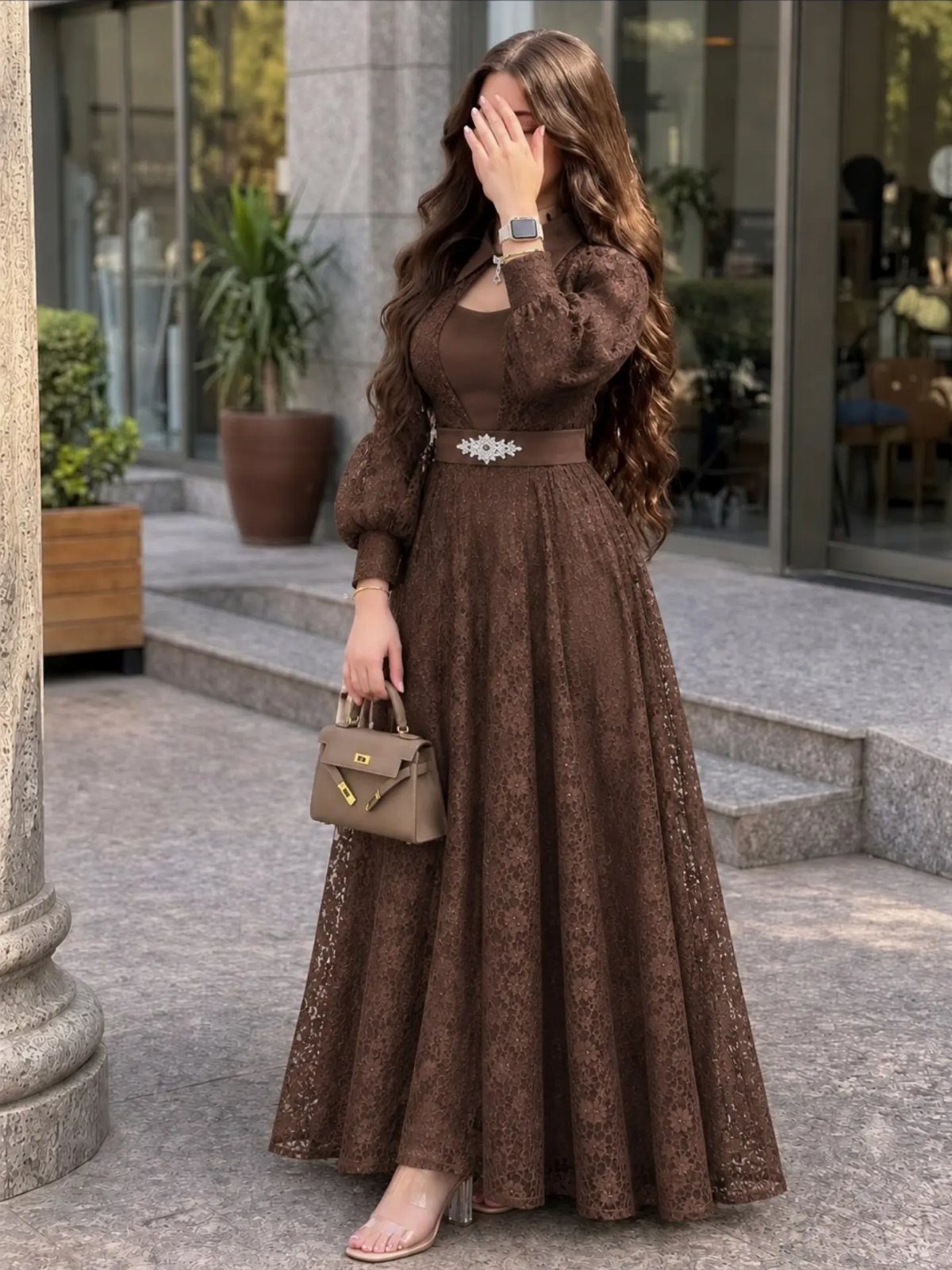 Woman wearing a long-sleeved brown lace maxi dress with a belted waist.