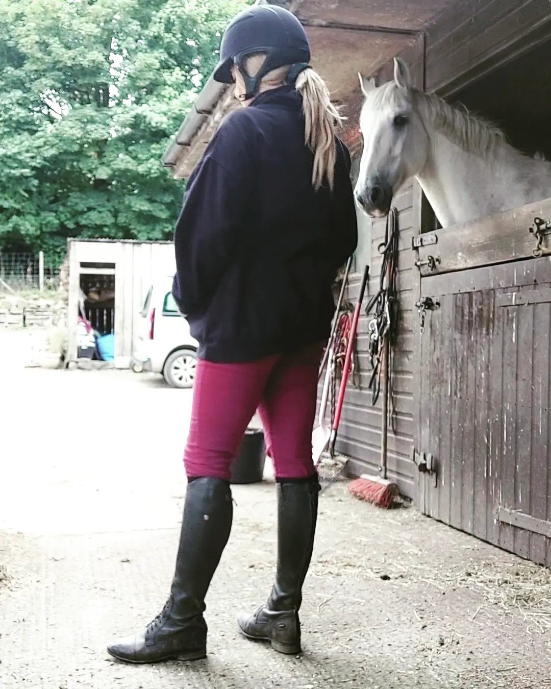 Woman in riding gear standing by a white horse in a wooden stable.