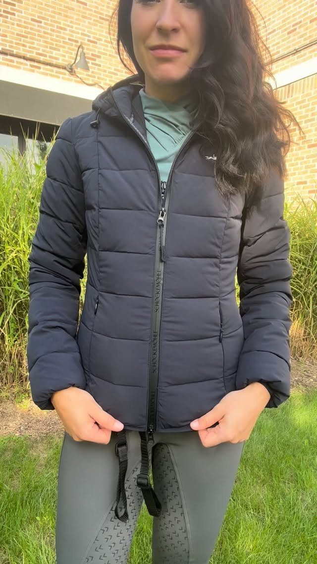 Woman wearing a navy puffer jacket and grey riding breeches outdoors.