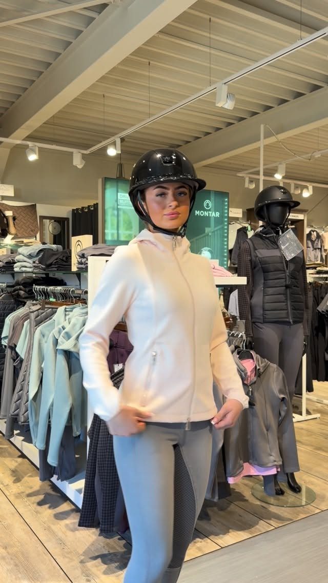 Woman wearing a riding helmet, pink jacket, and grey breeches in a store