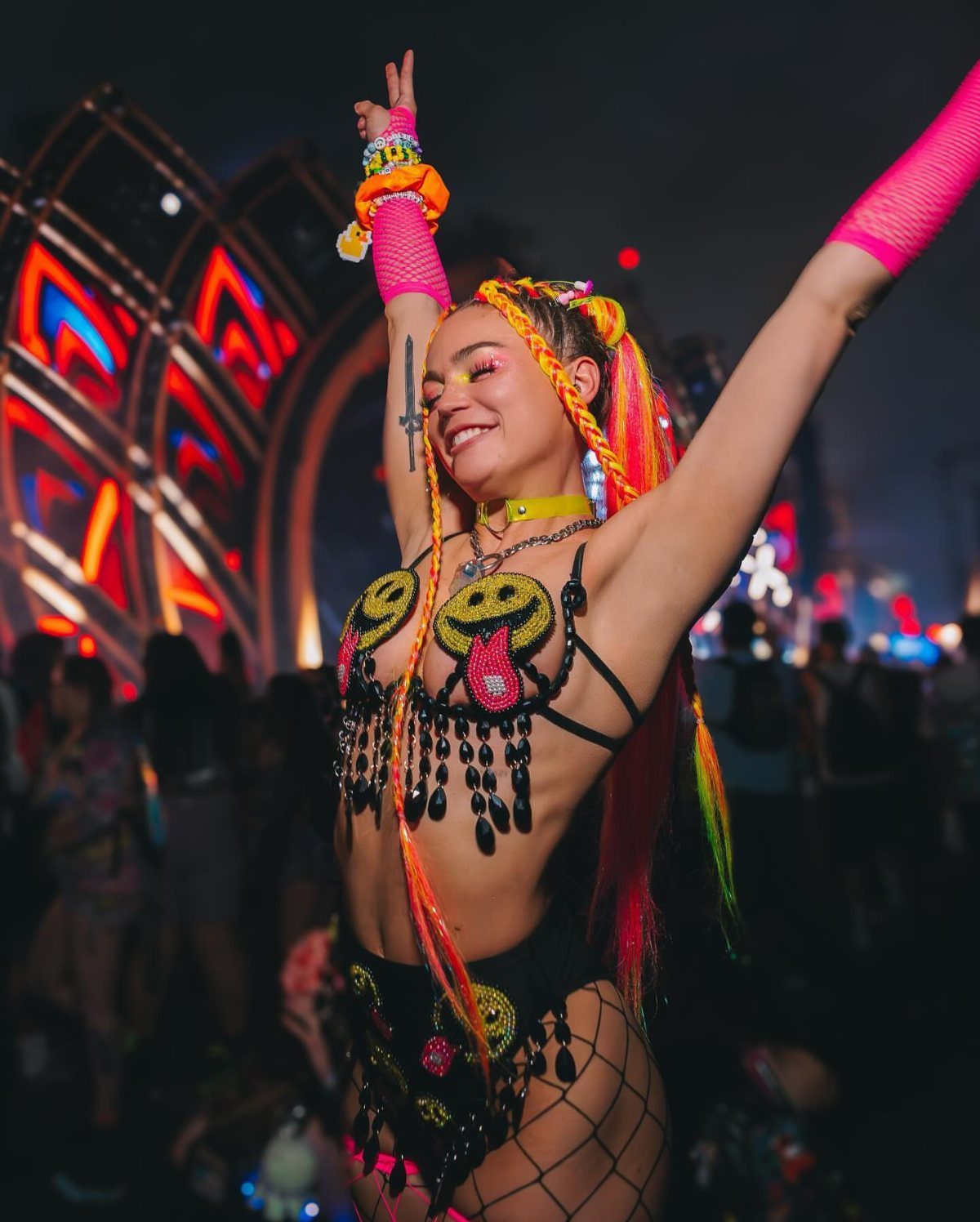 10 Woman Rave Outfit Ideas for Festival Nights 3 Woman in neon rave outfit with fishnet stockings and colorful braided hair extensions.