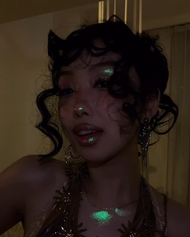 10 Woman Rave Outfit Ideas for Festival Nights 5 Woman with dark curly hair wearing iridescent glitter makeup on her face and chest.