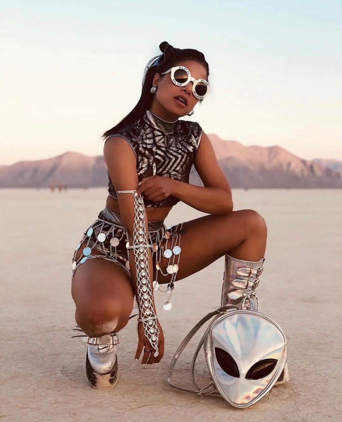 10 Woman Rave Outfit Ideas for Festival Nights 7 Woman in silver metallic rave outfit and alien bag in a desert setting