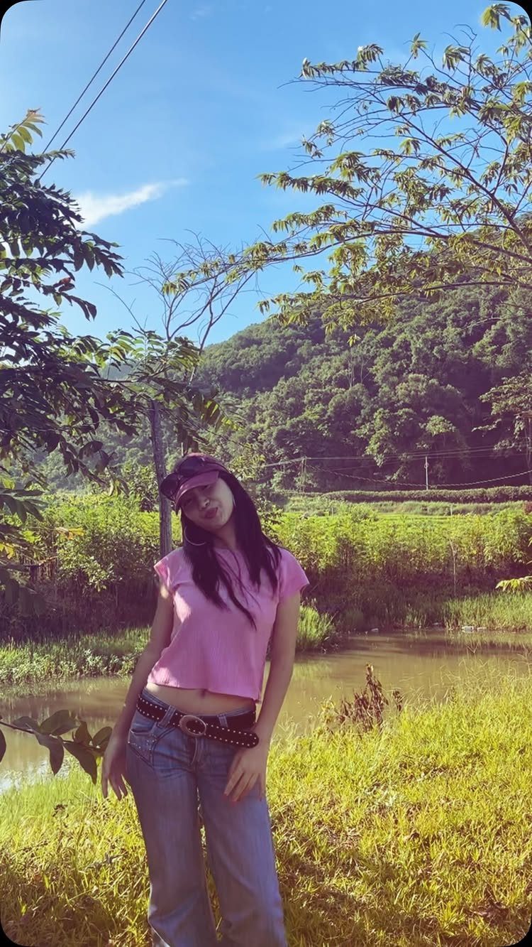 Woman in pink baby tee and low rise jeans standing in a sunny field